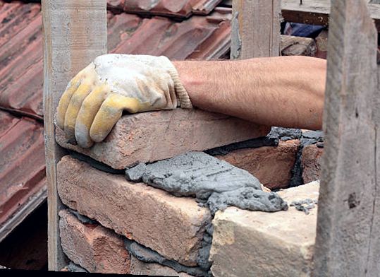 Mason laying a brick course with fresh mortar