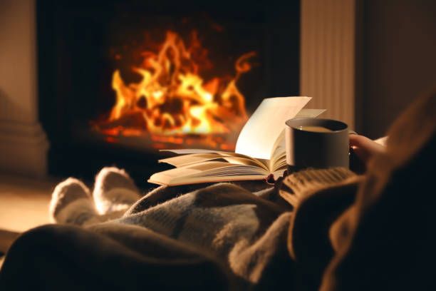 Reader by a glowing restored fireplace with a book and mug
