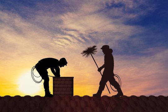Two chimney sweeps silhouetted against the sunset on a Montclair rooftop
